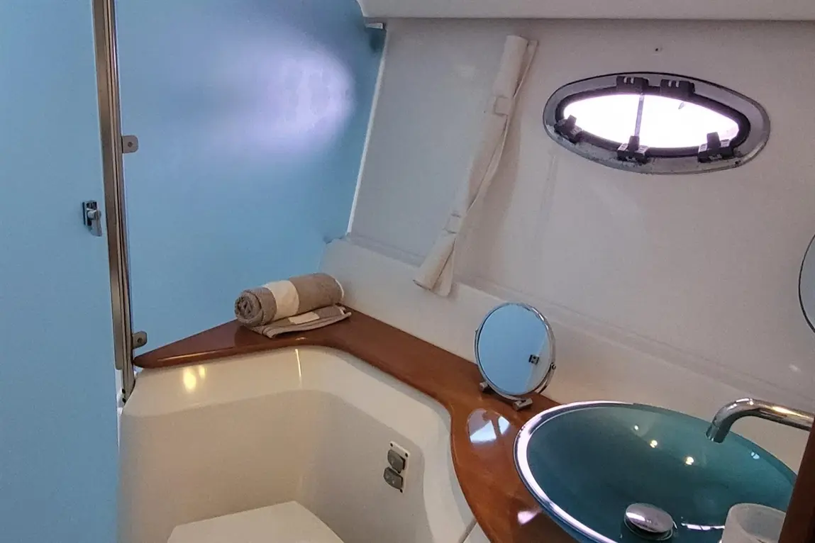 Compact bathroom interior with a blue wall, wooden countertop, a round mirror, and a turquoise sink, towels neatly arranged.